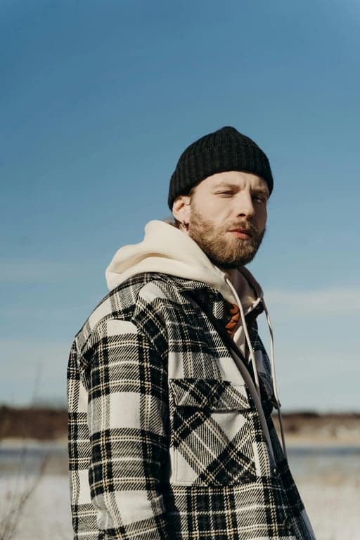 a portrait of a person transformed into a DC Comics–style comic illustration with sharp ink outlines, angular facial features, dramatic shadow blocks, saturated colors, and a serious superhero tone