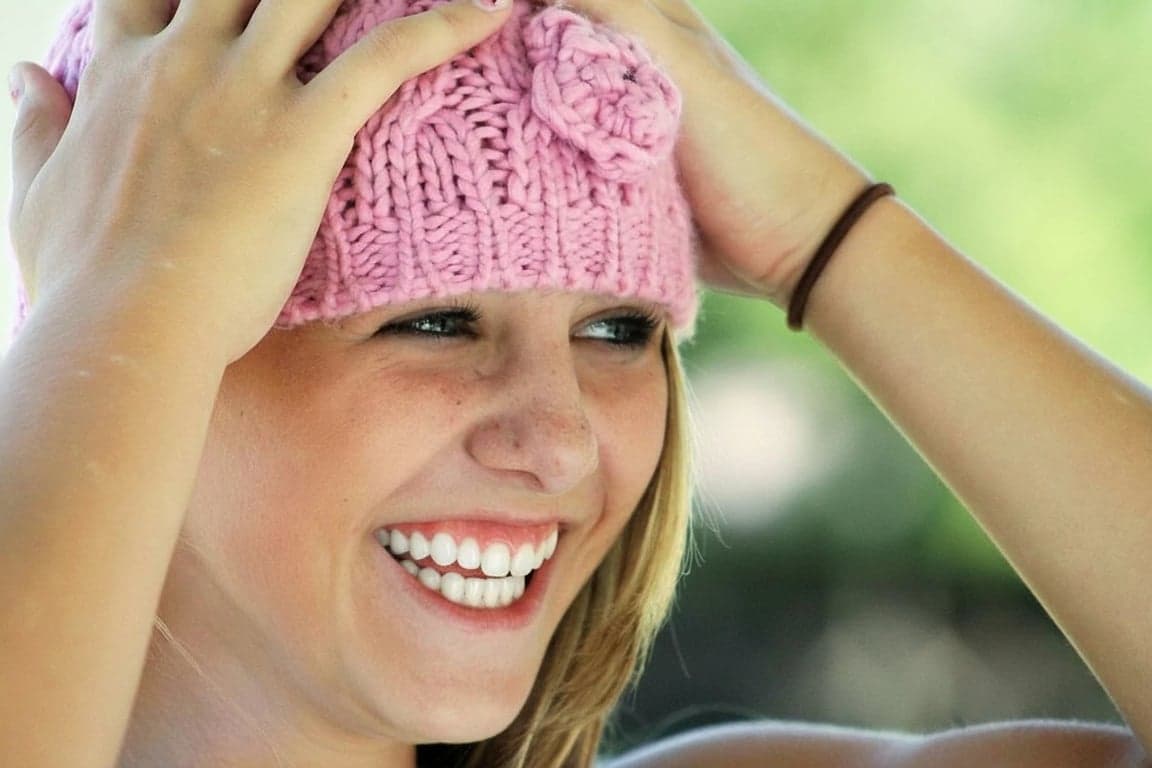 AI teeth whitening filter after photo - woman in pink hat smiling with brightened white teeth