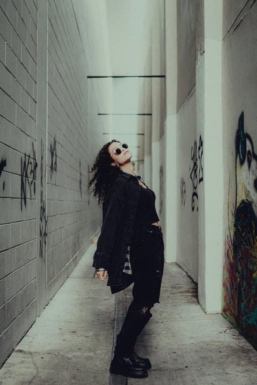 Transform the original person into a high-impact GTA character poster illustration by pushing graphic intensity. Maintain recognizability, but sharpen facial angles, deepen shadow blocks, and increase color saturation beyond realism. Use poster-style composition, strong directional lighting, and painterly yet graphic rendering so the character feels like a promotional GTA character reveal, not a softened illustration.