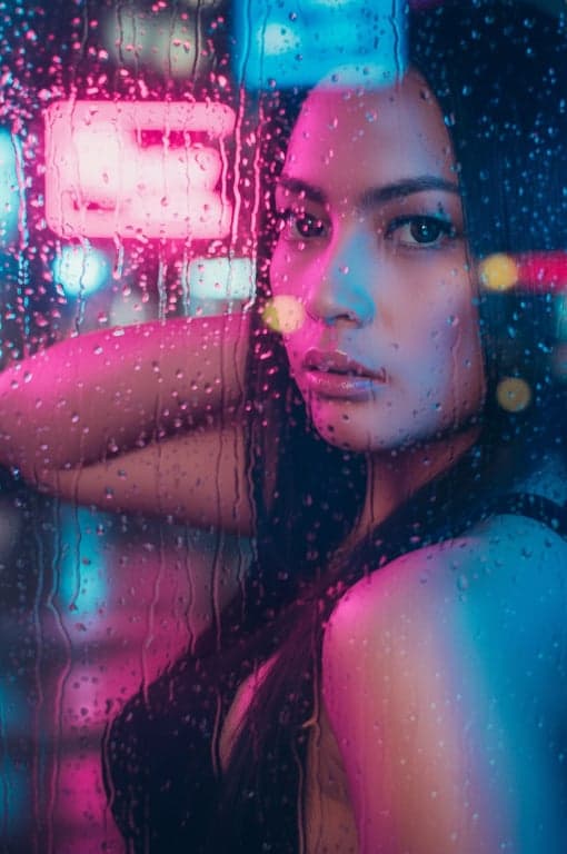 a portrait of a person with a cyberpunk neon glow filter, face illuminated by vibrant pink and blue neon signs, with rain streaks on glass