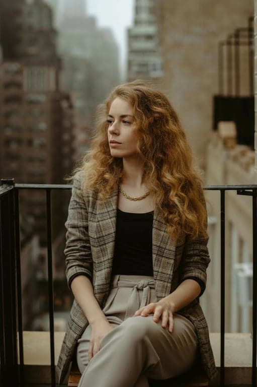 a portrait of a person edited to sit comfortably with one leg crossed over the other, upper body relaxed, shoulders dropped, chest open, neck uncompressed; avoid exaggerated posing; preserve anatomy and clothing folds; background unchanged; result should look naturally composed