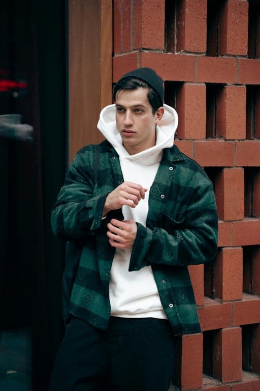 Reinterpret the original person as a cinematic GTA action illustration by exaggerating contrast, perspective, and attitude. Preserve identity cues, but emphasize harsh light–shadow separation, angular facial structure, and dynamic visual tension. Apply cinematic color grading, strong highlights, and bold linework so the image feels like a dramatic freeze-frame from a GTA storyline rather than a static portrait.