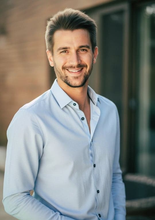 A professional AI-generated resume photo of a man, mid-shot, wearing a collared shirt, warm smile, natural skin tone, soft blurred background, approachable yet competent.