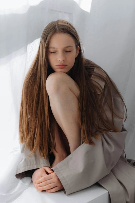 Wolf cut filter before pic – woman sitting indoors with long straight hair and neutral coat