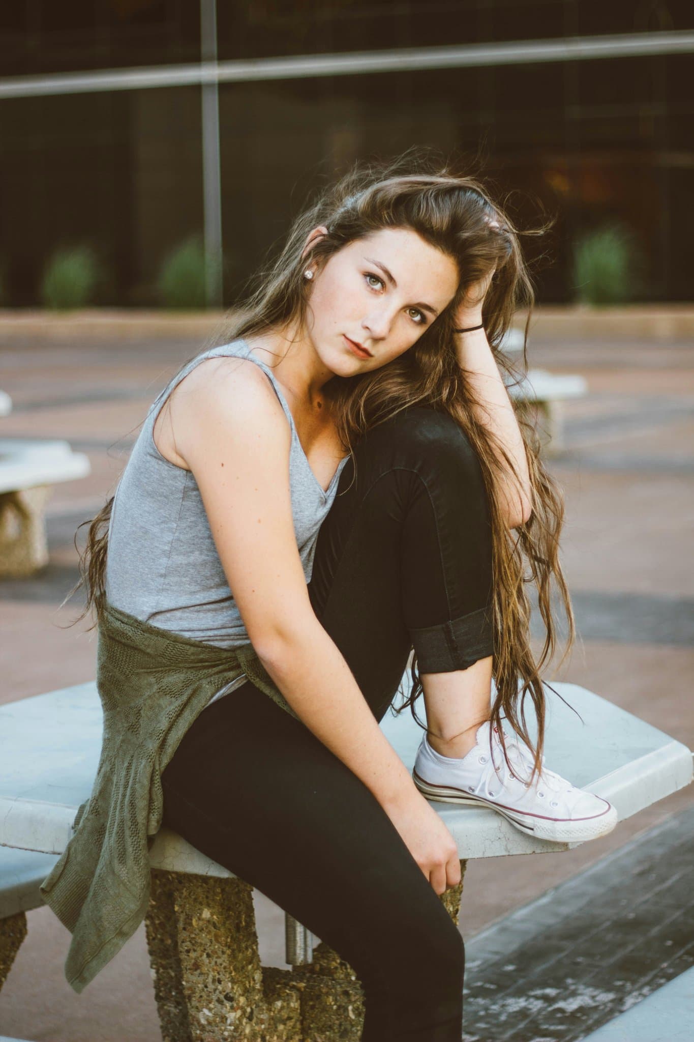 Casual outfit with tank top and black pants, seated outdoors with natural, slightly serious expression.