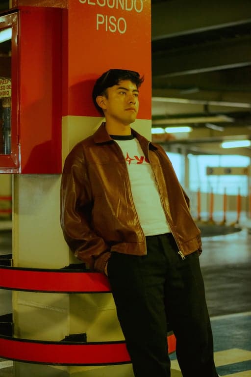 Render the original person as a definitive GTA V loading screen illustration, prioritizing iconic graphic stylization over realism. Preserve facial identity and pose, but aggressively flatten textures into painted color blocks, exaggerate facial planes, and apply thick, high-contrast contour lines. Use bold saturated colors, dramatic rim lighting, and simplified illustrated backgrounds so the result unmistakably resembles official GTA loading screen artwork rather than a realistic portrait.