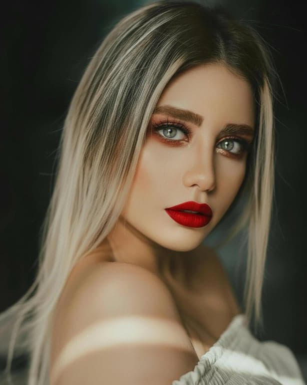 A high contrast color portrait of a woman, vibrant red lips against muted skin tones, dark defined eyebrows, sharp details, plain dark background.