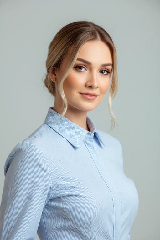 A polished CV headshot of a woman, professional blouse, hair styled neatly, slight head tilt, bright and inviting eyes, light grey studio backdrop.