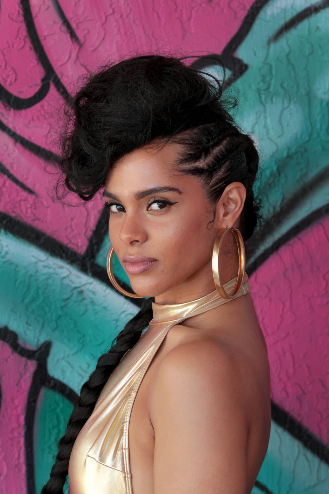 Bold graffiti wall setting with sculpted hairstyle and metallic gold halter top.