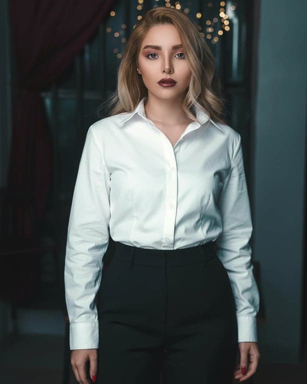 a portrait of a person in a minimalist monochrome outfit with tailored shirt and straight trousers, crisp structure, understated construction, refined simplicity, balanced posture, gentle daylight