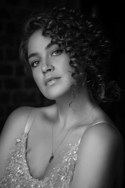 A dramatic high contrast black and white portrait of a woman, pure white eyes, deep black hair, strong facial contours, studio lighting.